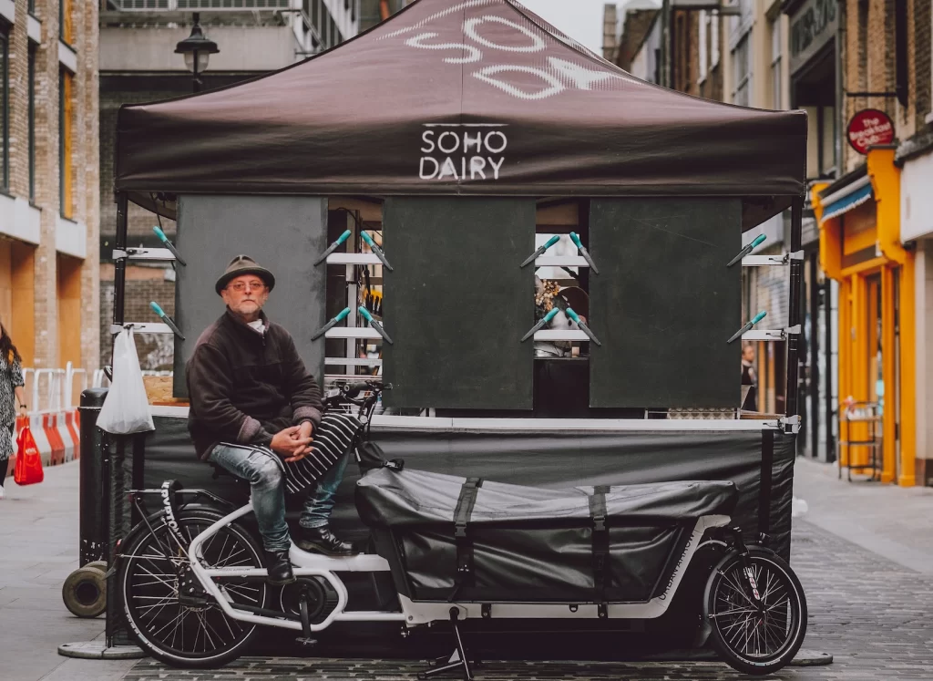Robin at the stall Soho Dairy's founder Robin sits on his electric cargo delivery bike at the market stall on Berwick Street Market.