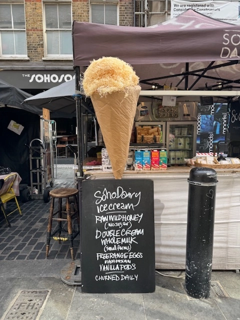 An image showing a large handmade prop ice cream cone and signage board at the Soho Dairy stall to promote Soho Dairy raw honey ice cream